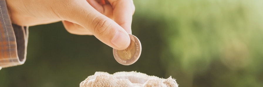 hand puting coins in money bag for saving on table background 