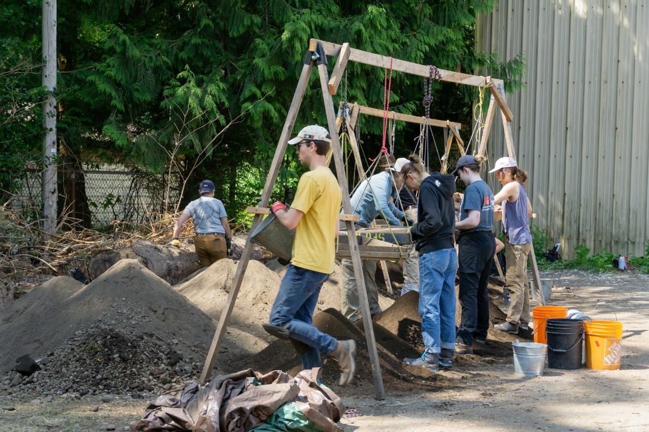 A group of students stand and sift through sediment to find artifacts