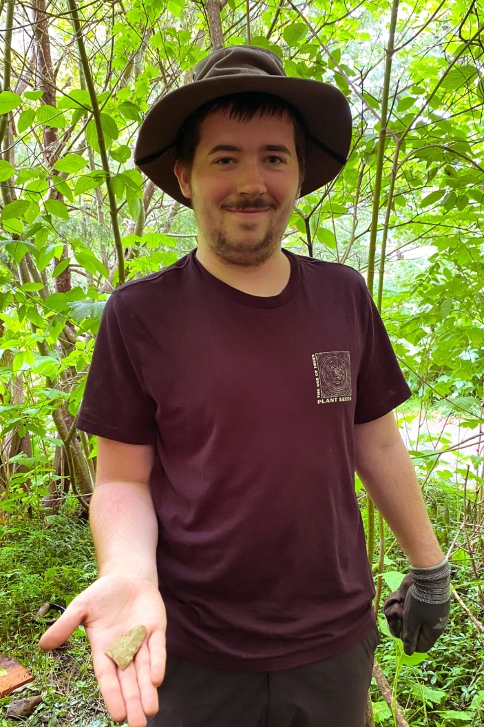 Evan Mugford smiles while holding an artifact in outstretched palm