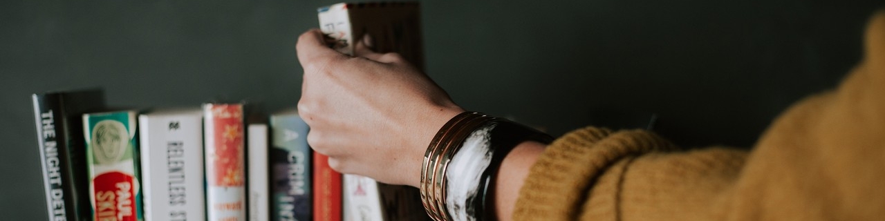 A hand reaching for a book on a bookshelf