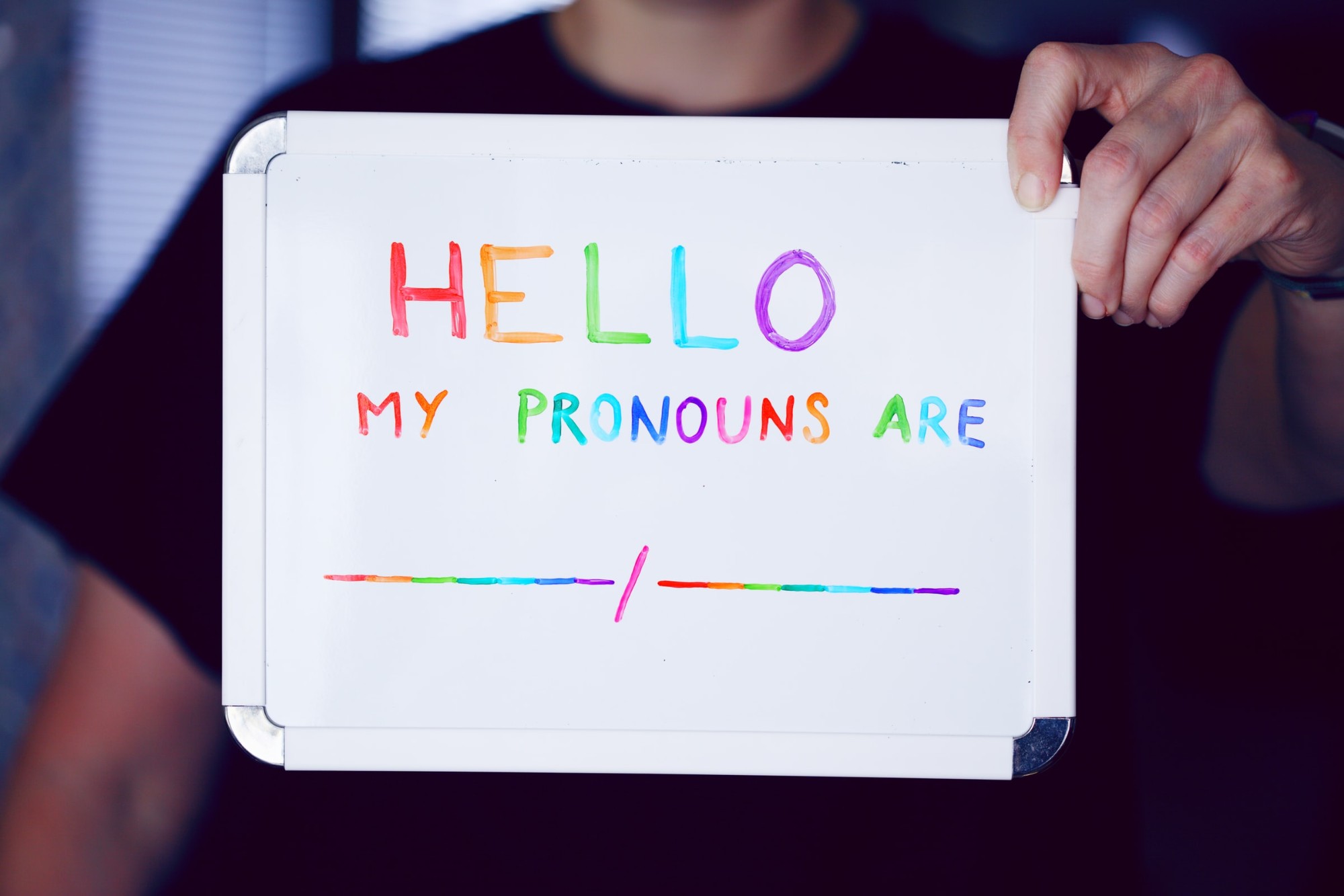A person holding up a whiteboard that says "Hello my pronouns are"