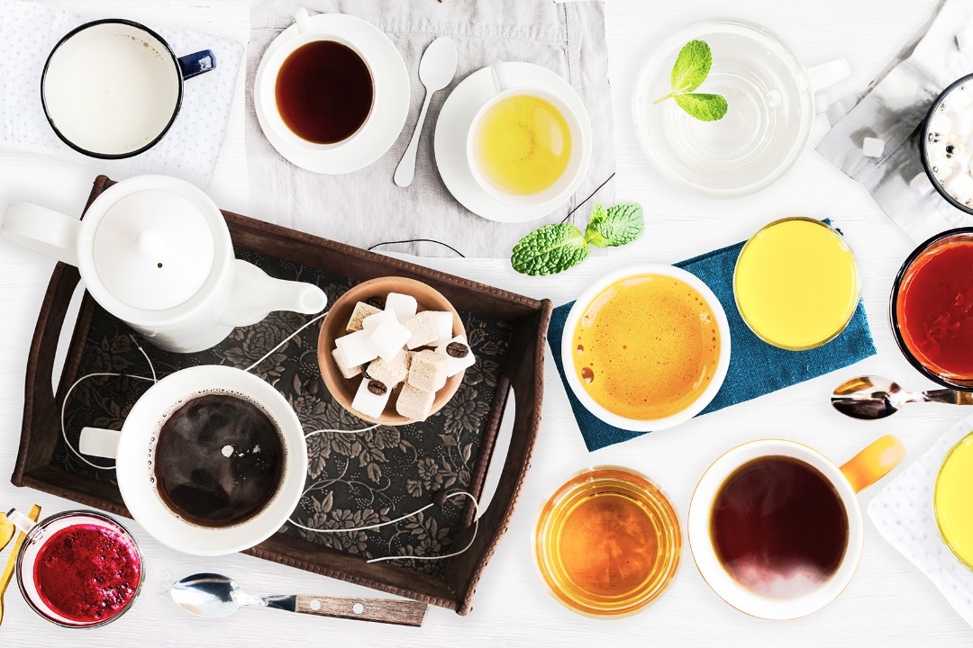 Set of different cold drinks and hot drinks - juices, coffee, tea, milk, mint water - cups and mugs served on white wooden table. Closeup. Top view.