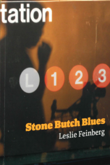 Book cover for Stone Butch Blues by Leslie Feinberg. The title is written in bold yellow letters, with the author's name below in white. The background image features a shadow of a person and their bike against the sign of a subway station.