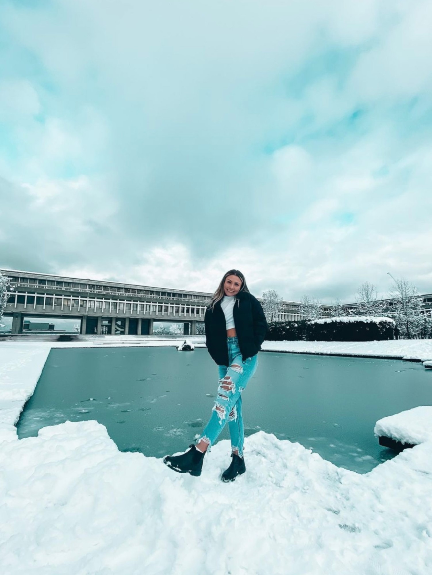 Alexia is standing near the AQ pond during the winter. Water is froze and snow all around. Smiling at the camera