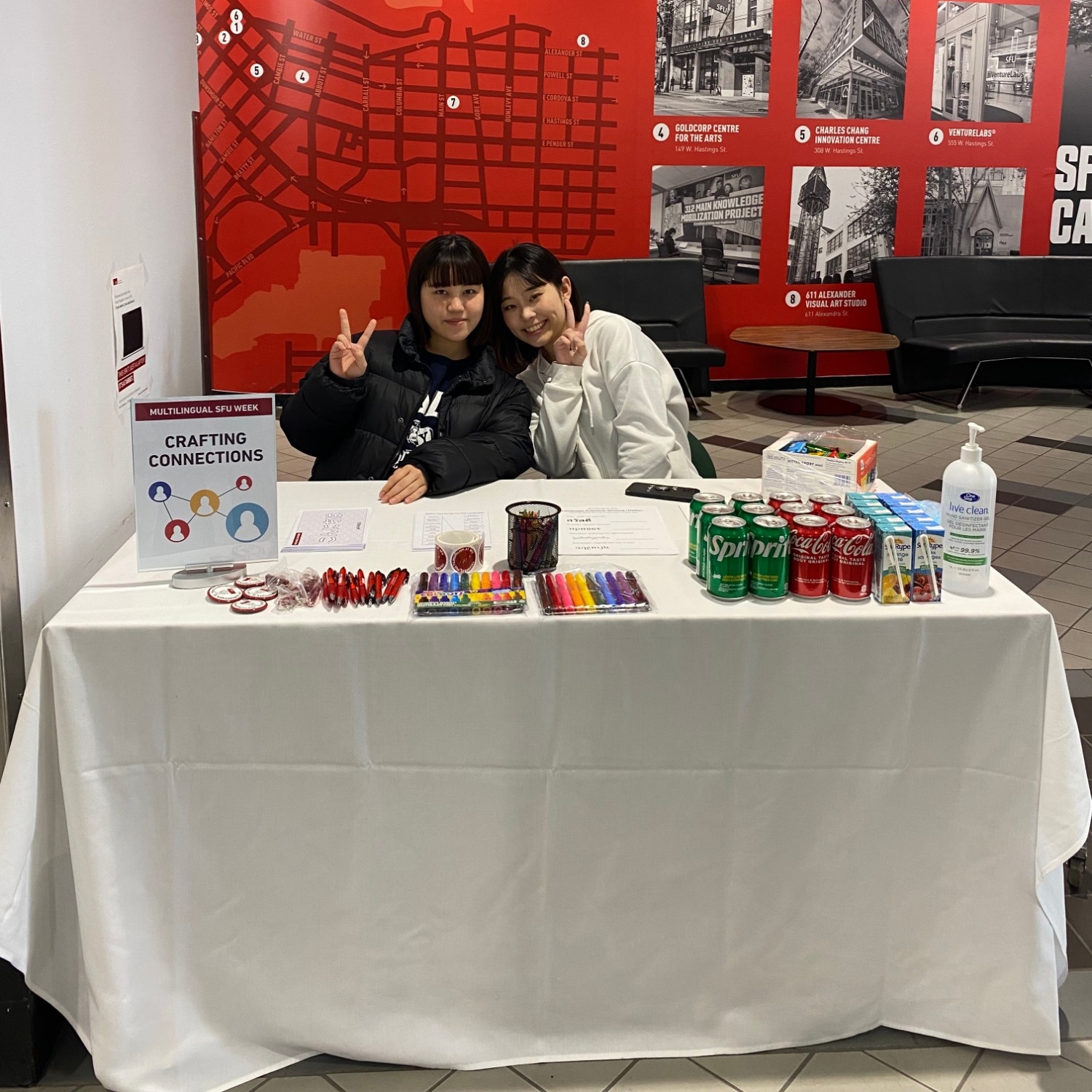 Two students sitting at a table and giving away snacks and prizes as part of a crafting connections activity for Multilingual Week 2023 at Vancouver campus