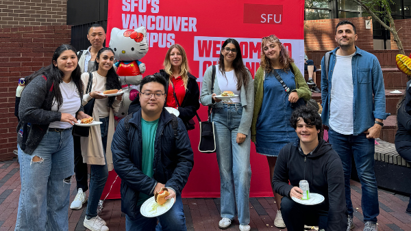 Group of students smiling in front of a red banner at the 2024 SFU Vancouver Welcome Back Community BBQ