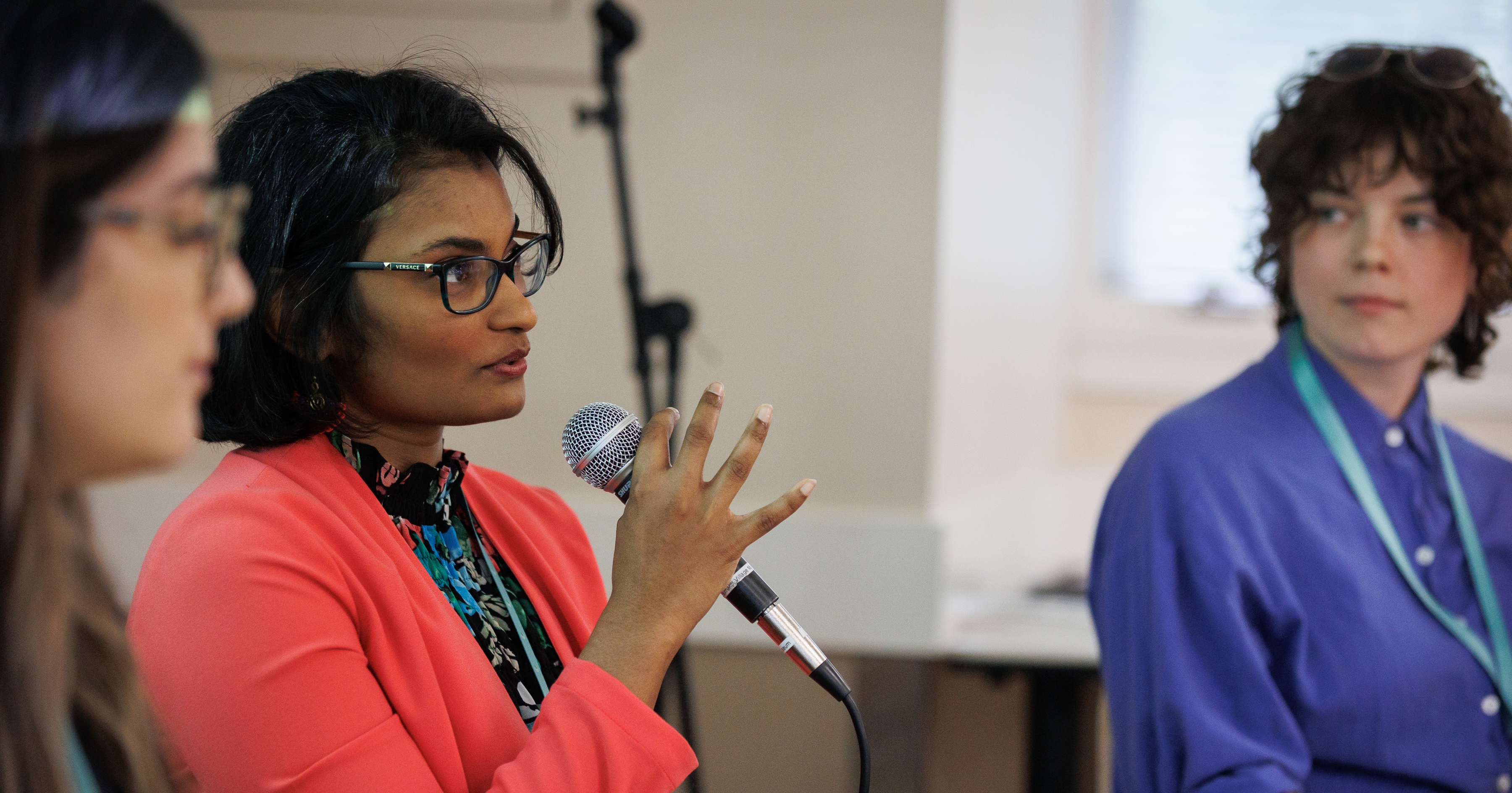 A woman with bright red cardigan holding a mic.