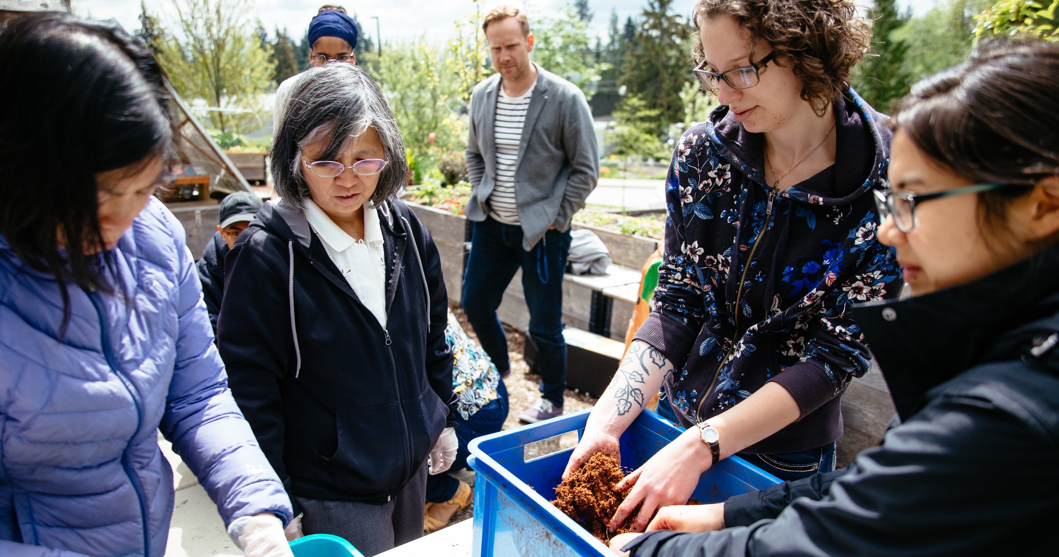 People standing up looking at a blue container full of fertilizer.