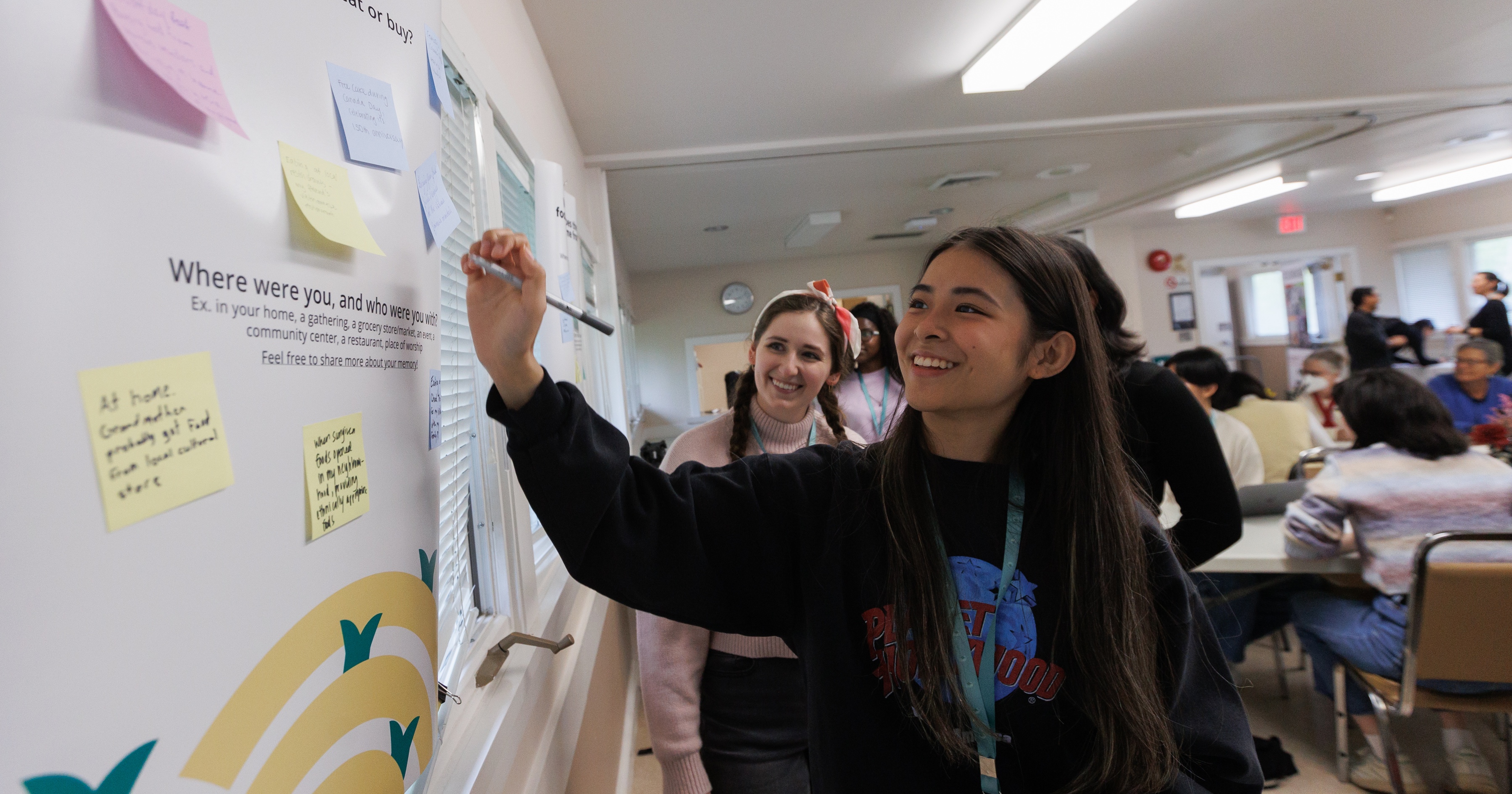 Two women smiling and writing on a whiteboard full of post its. 