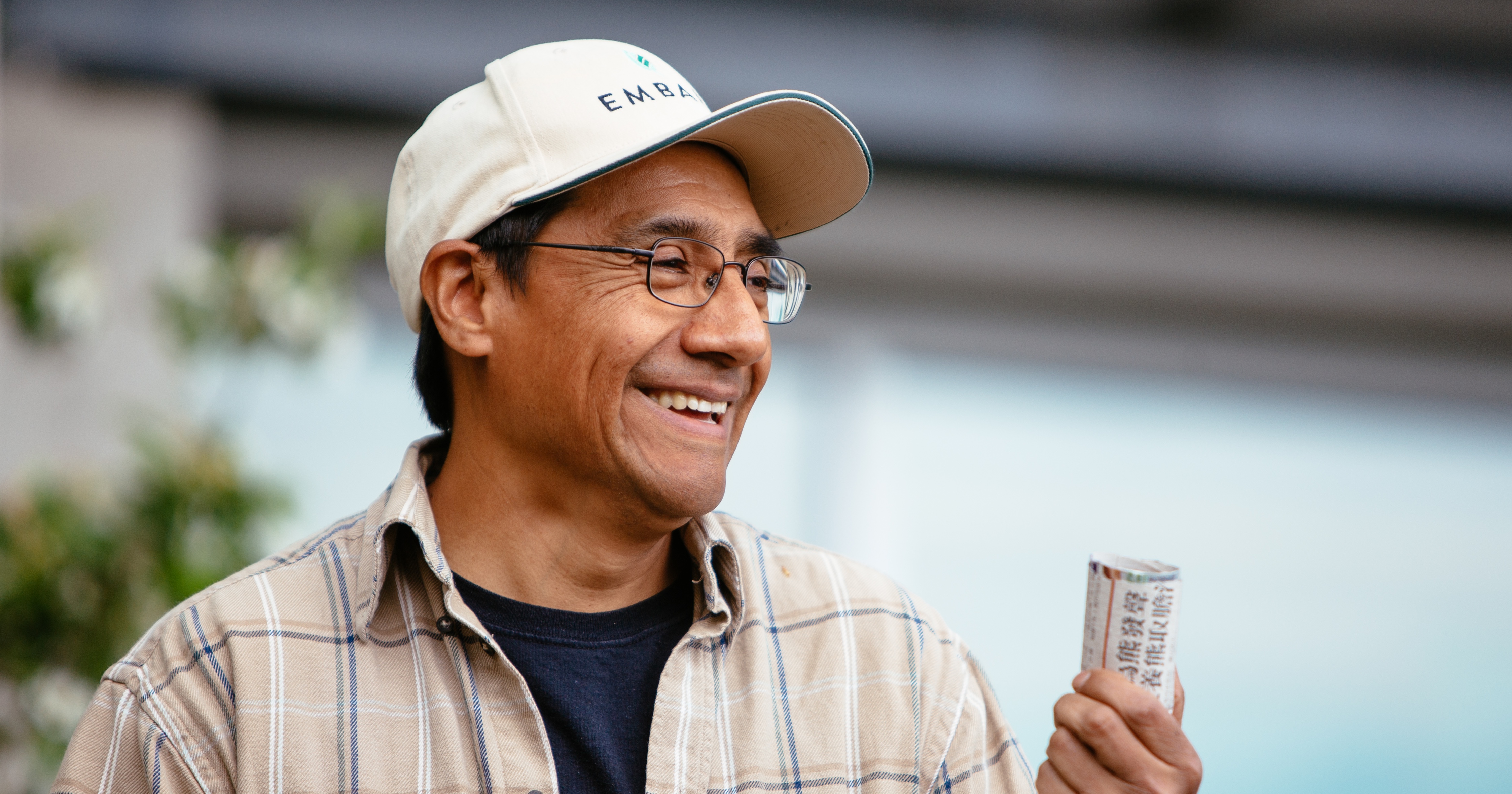 A man with a cap and glasses holding a cylindrical bottle.