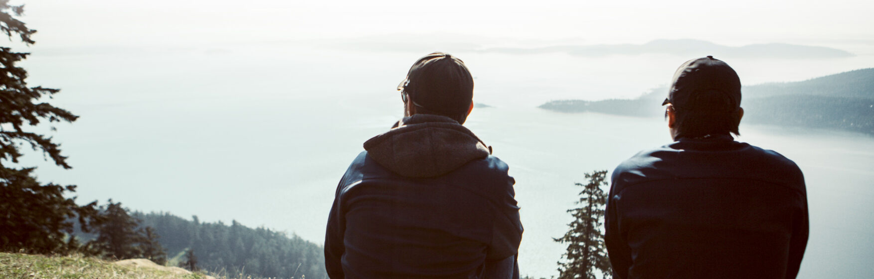 Two men sitting on a cliff, looking into the ocean