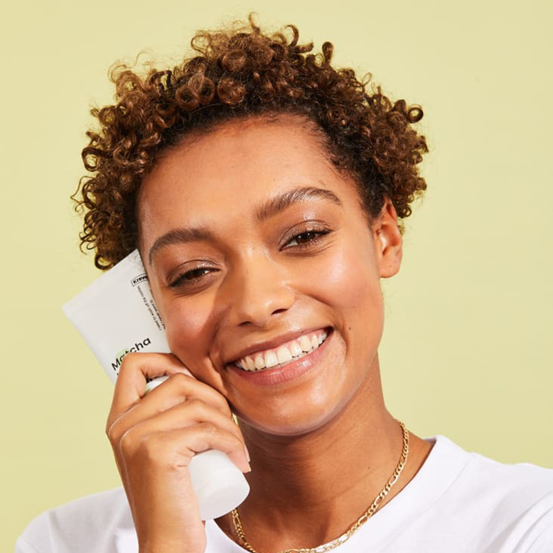 A women holding Matcha Hemp Cleanser on the side of her face