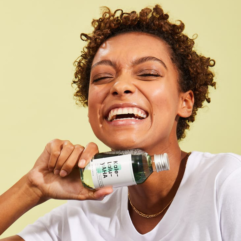 A woman smiling and holding a bottle of Kale-Lalu-yAHA