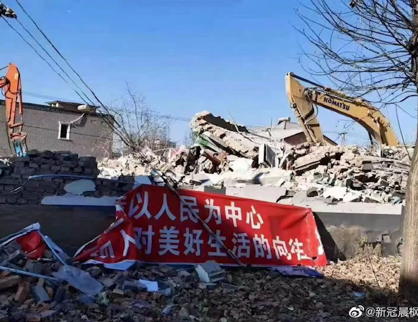 first posted image, showing a ruin, a propaganda slogan poster and an excavator. the propaganda slogan says '...put people's need at the center...for people's hope for a better life.