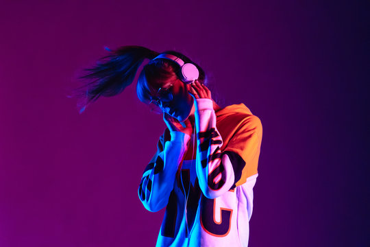 a women listening to music on her headphones in fron ot violet background, shaking her hair