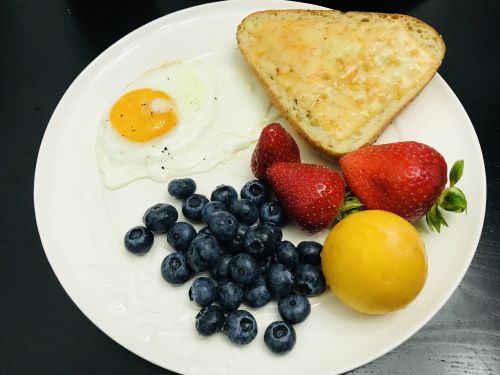 Breakfast with fried-egg, bread and chesse, strawberries, a plum and blueberries.