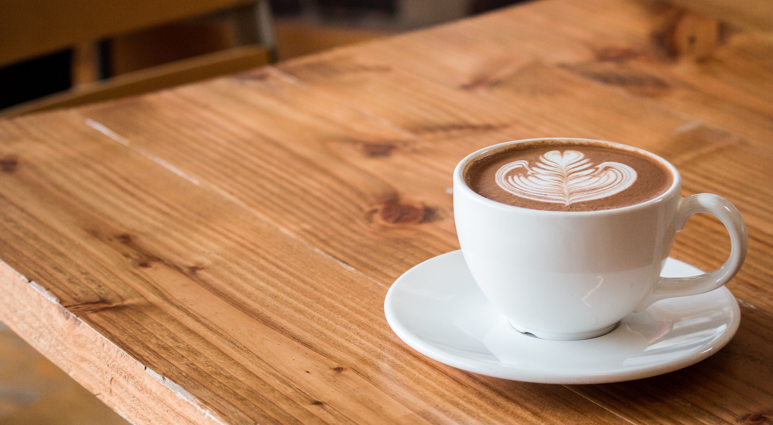 wide image of coffee with foam art in white mug on tea plate on wood table