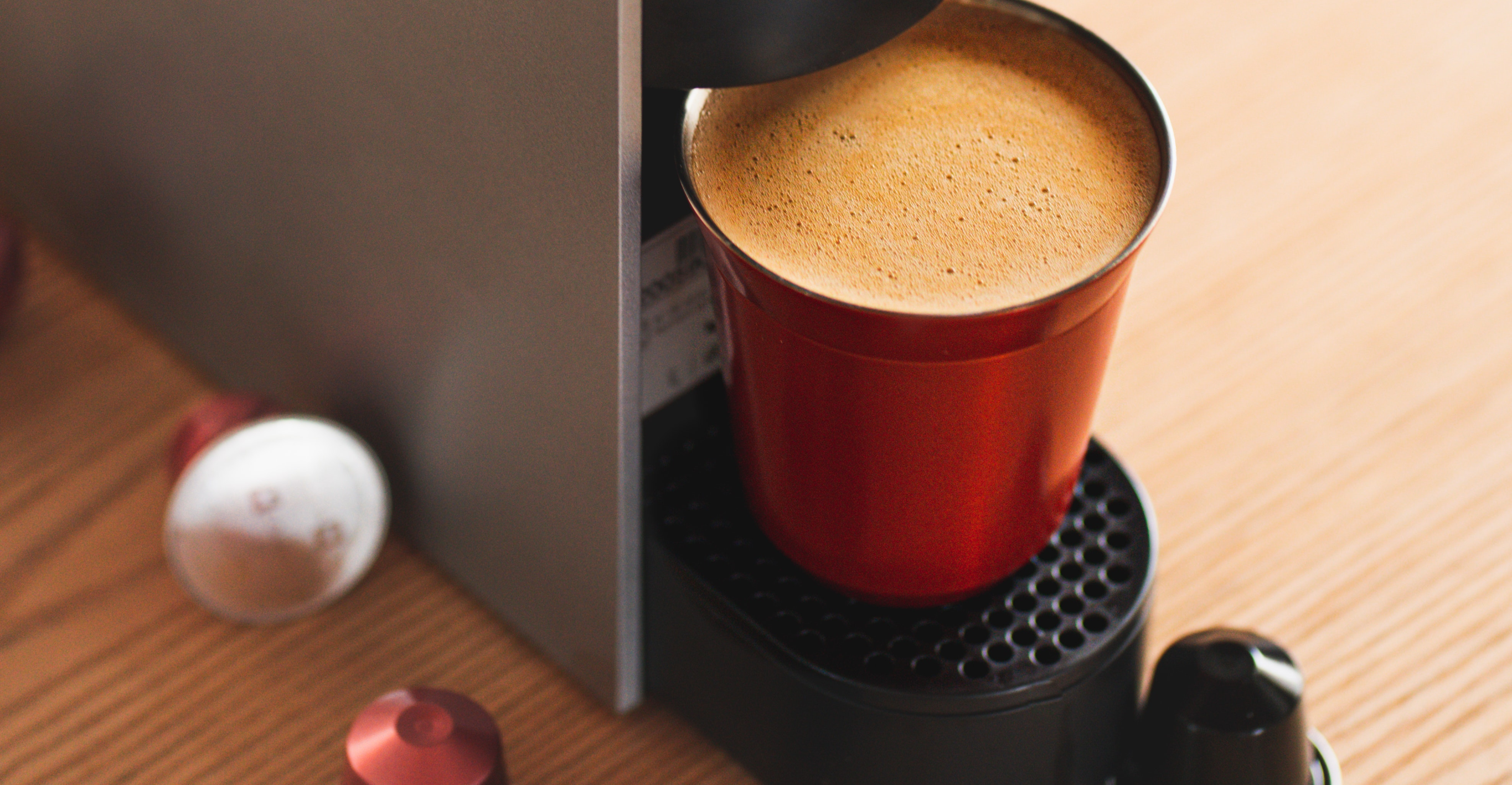 wide image of single serve coffee maker with a yellow mug and pods