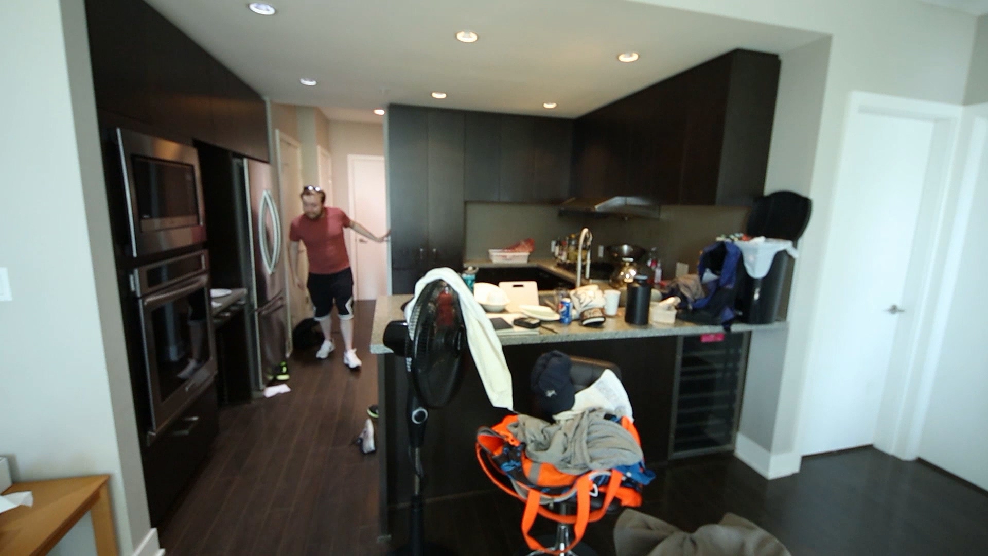 A man standing in the corridorbeside the kitchen and the room is mess up.