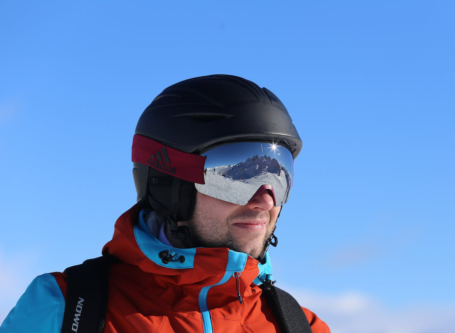 orange jacket skiier wearing a black helmet in clear skies