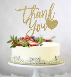 a fancy white cake with berries and a sign saying thank you