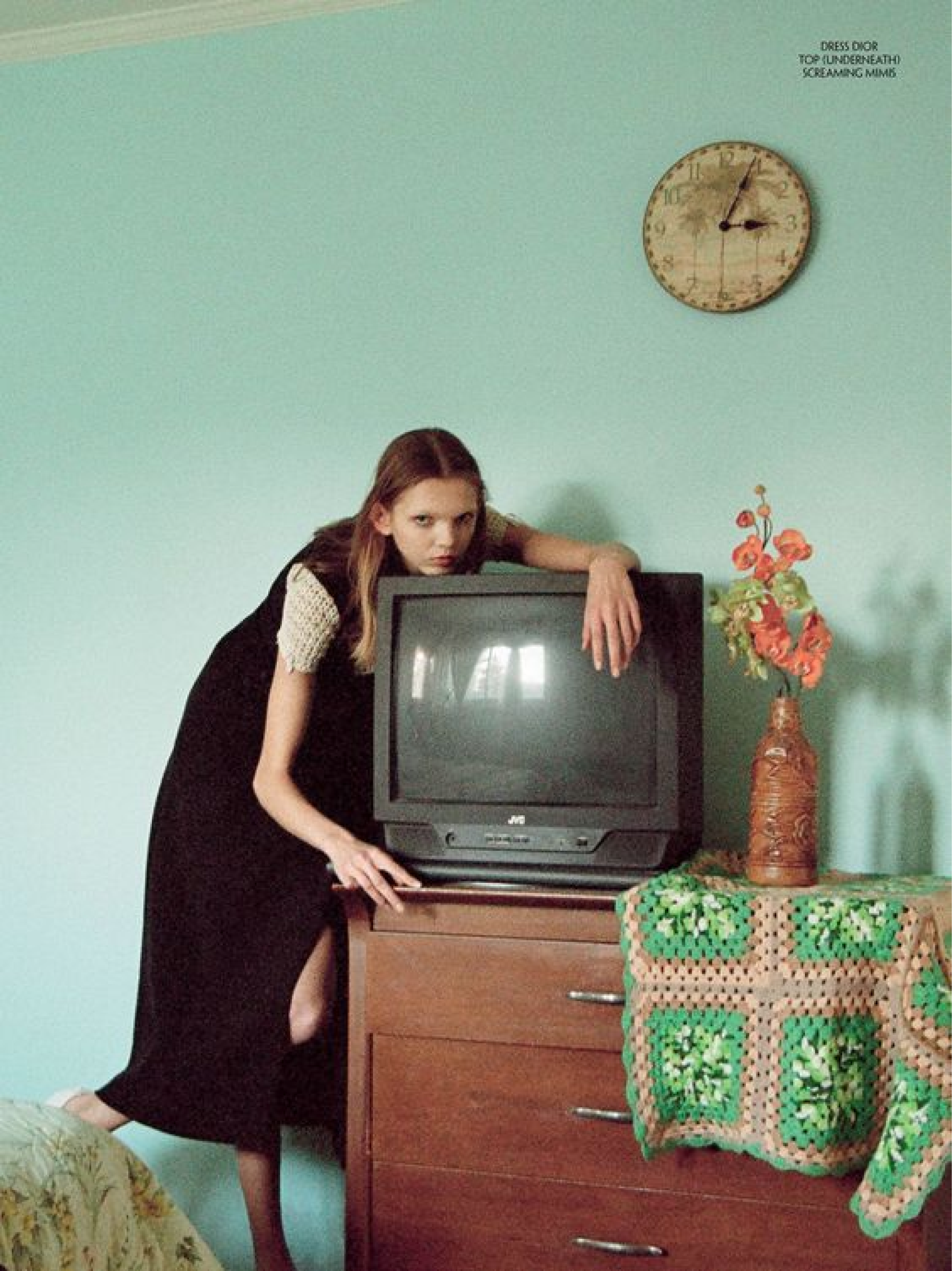 A female model is lying on a television in a green living room.