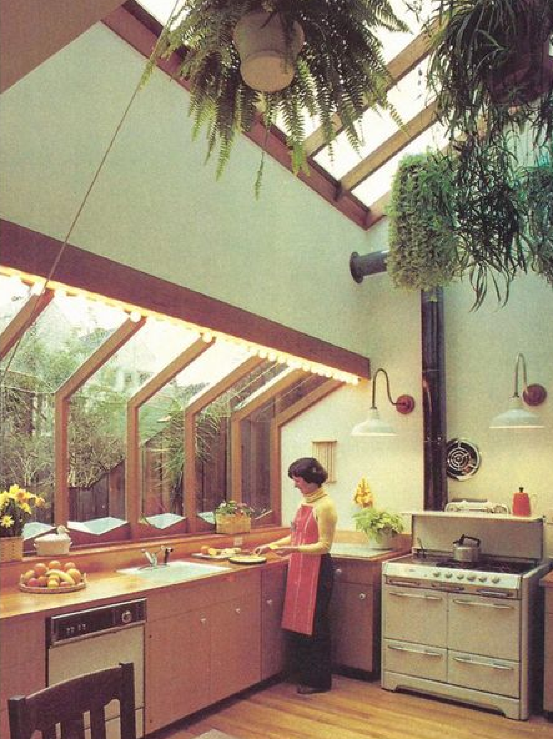 A woman is placing fruits on a plate in a 1980s design kitchen with green plants decoration at the celling.