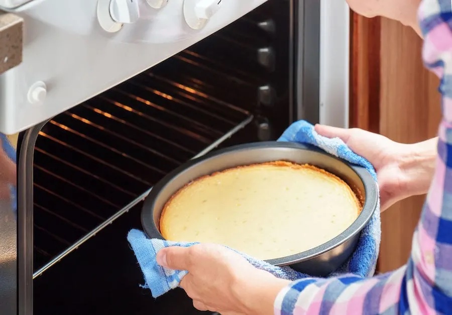 A person putting cheesecake in the oven.