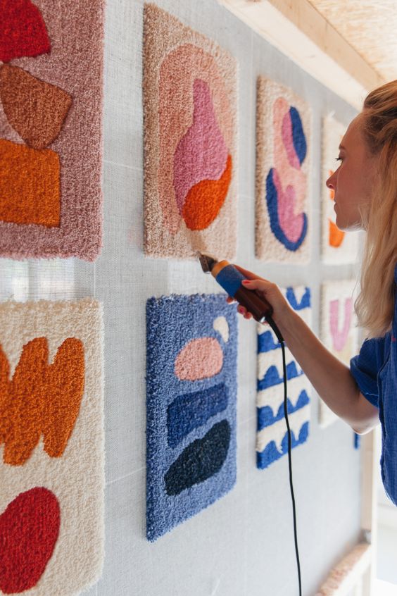 An artist trimming a rug on a standing canvas with multiple rugs