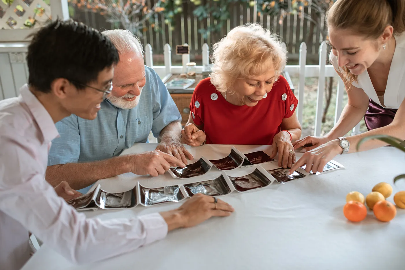 Four smiling people sit around a table looking at several old pictures spread out.